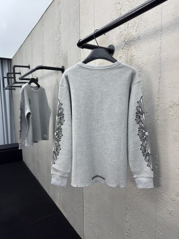 Maglione grigio elegante con ricami floreali, su asta minimalista in ambiente industriale moderno.