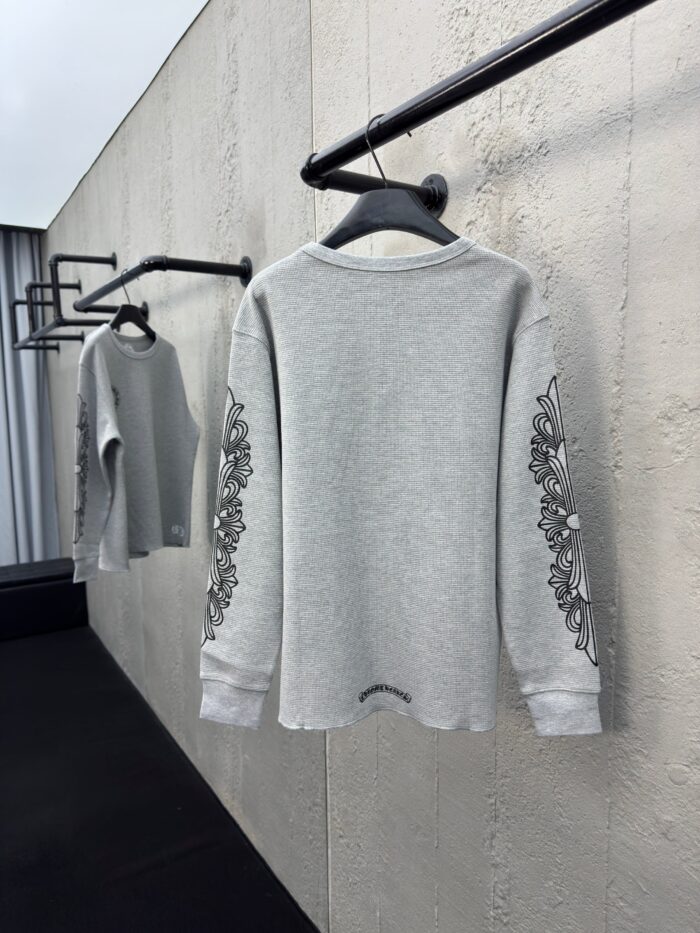 Maglione grigio elegante con ricami floreali, su asta minimalista in ambiente industriale moderno.