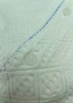 Copriletto bianco imbottito con dettagli blu e bottoni trasparenti, tessuto morbido e elegante.