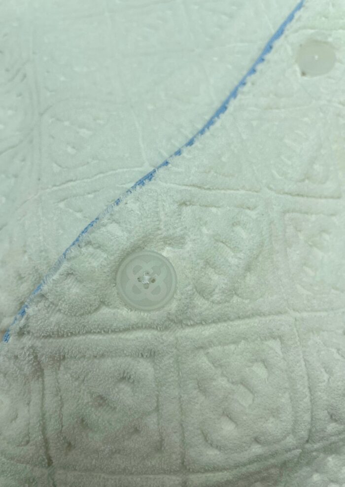 Copriletto bianco imbottito con dettagli blu e bottoni trasparenti, tessuto morbido e elegante.
