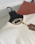 Maglione beige in cotone su gruccia nera con etichetta di lusso, sfondo minimalista naturale.