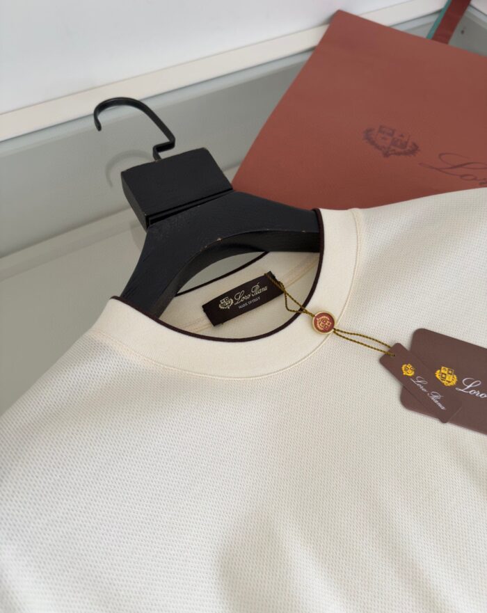 Maglione beige in cotone su gruccia nera con etichetta di lusso, sfondo minimalista naturale.