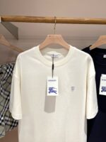 Maglietta cream con logo ricamato Burberry, elegante e versatile, esposta su appendiabiti in negozio.