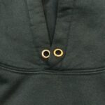 Felpa verde scuro con occhielli in metallo dorato e dettaglio di ventilazione.