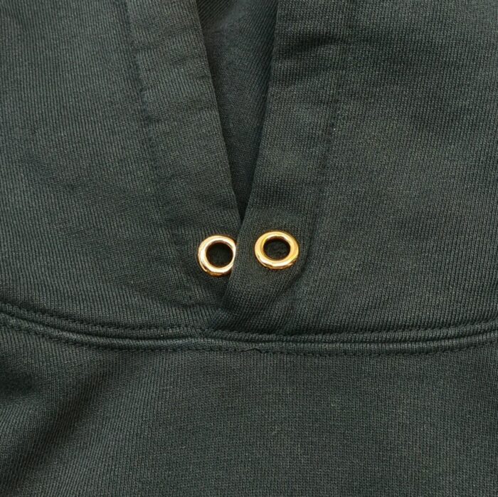 Felpa verde scuro con occhielli in metallo dorato e dettaglio di ventilazione.