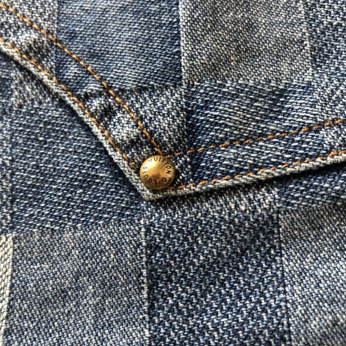 Dettaglio denim plaid con rivetto in ottone e cuciture beige, stile vintage e qualità artigianale.