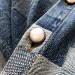 Dettagli denim con bottone lucido, cuciture marroni e texture particolare.