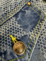 Jeans in denim houndstooth con bottone Louis Vuitton e cuciture gialle a contrasto.