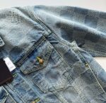 Giacca in denim chiaro con pattern a griglia, bottoni dorati e dettagli moderni.
