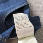 Etichetta di cura jeans in denim con materiali e istruzioni multilingue.