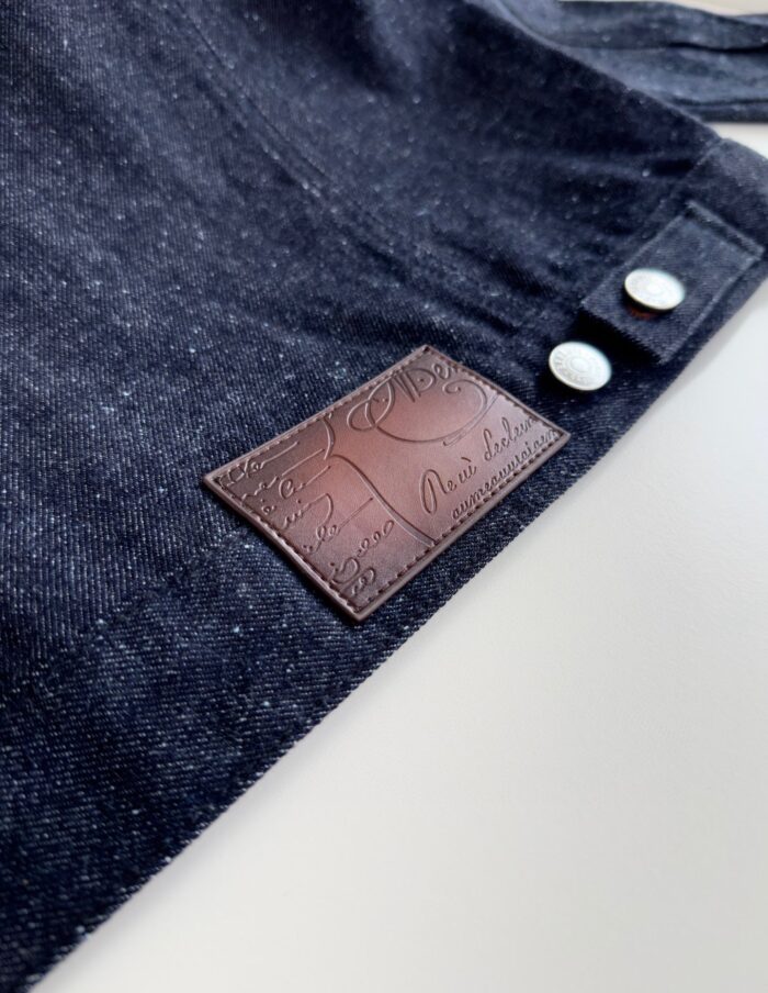 Grembiule in denim con dettagli in pelle e bottoni bianchi per stile e praticità.