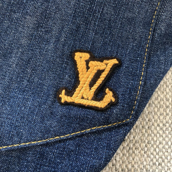 Emblema LV ricamato su jeans in denim blu vintage, simbolo di lusso e stile casual.