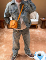 Stiloso outfit in denim con borsa arancione e sneakers colorati in ambiente moderno e accogliente.
