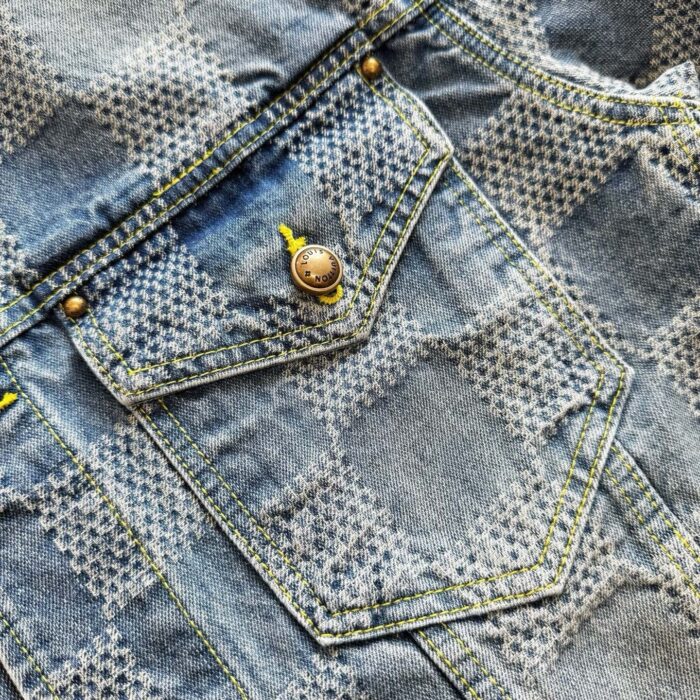 Tasca in denim chiara con bottone in ottone e dettagli di cuciture colorate.