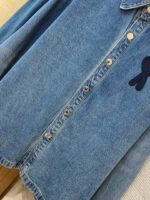 Camicia in denim chiara con bottoni metallici e ricamo blu, stile casual elegante.