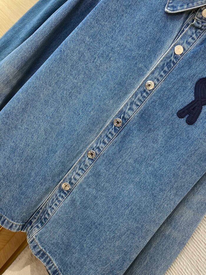 Camicia in denim chiara con bottoni metallici e ricamo blu, stile casual elegante.