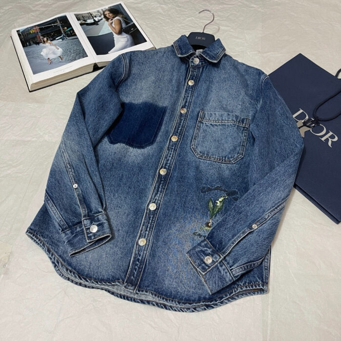 Camicia jeans di lusso con ricamo verde e dettaglio elegante, accompagnata da shopping Dior.