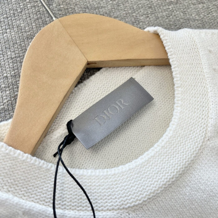 Maglione Dior beige in cashmere, con collo rotondo, su appendiabiti di legno elegante.
