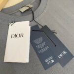 Maglietta grigia Dior con etichette di lusso, tessuto morbido e design minimalista elegante.