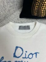 Maglione Dior in maglia avorio con dettagli artistici e logo blu elegante.