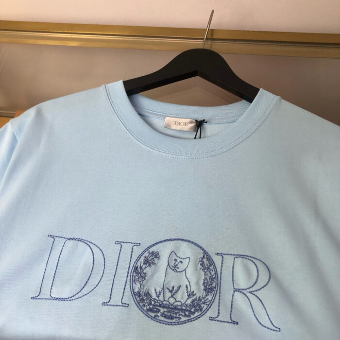 Maglietta Dior azzurro chiaro con logo e design artistico gatto, stile moderno e raffinato.