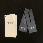 Etichetta Dior su abbigliamento nero, con logo bianco e dettagli di cura eleganti.
