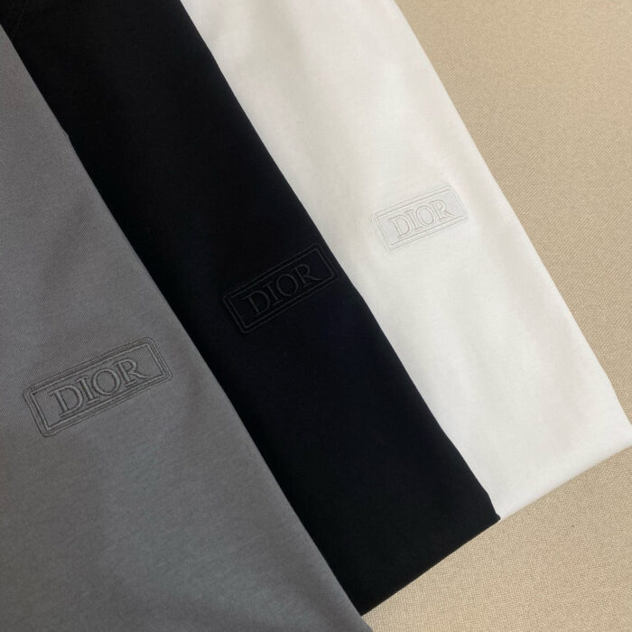 T-shirt Dior in colori neutri con logo embossato, elegante e minimalista su sfondo sabbia.