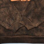 Felpa marrone con dettaglio arancione e texture naturale, stile casual e moderno.
