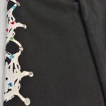 Tessuto nero con motivo bianco e gemme colorate, perfetto per abiti eleganti e accessori raffinati.