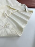Tessuto crema con pieghe delicate, dettagli artigianali e contrasti di colore caldo.