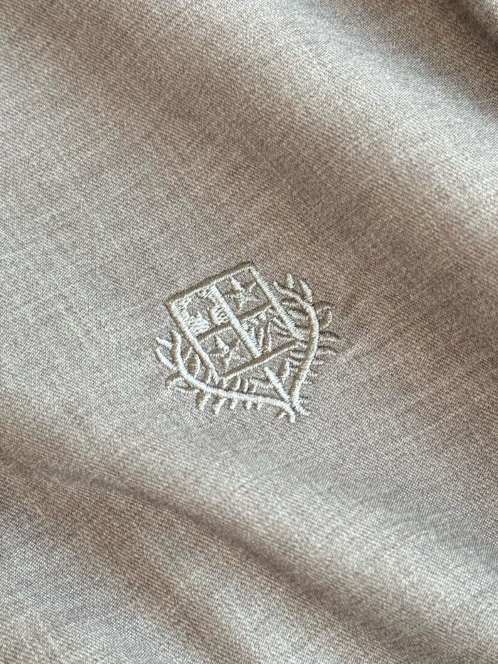 Tessuto elegante con ricamo di stemma heralico, dettagli raffinati e texture di alta qualità.