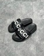 Sandali slide Gucci neri con logo bianco, stile casual e comfort di lusso.