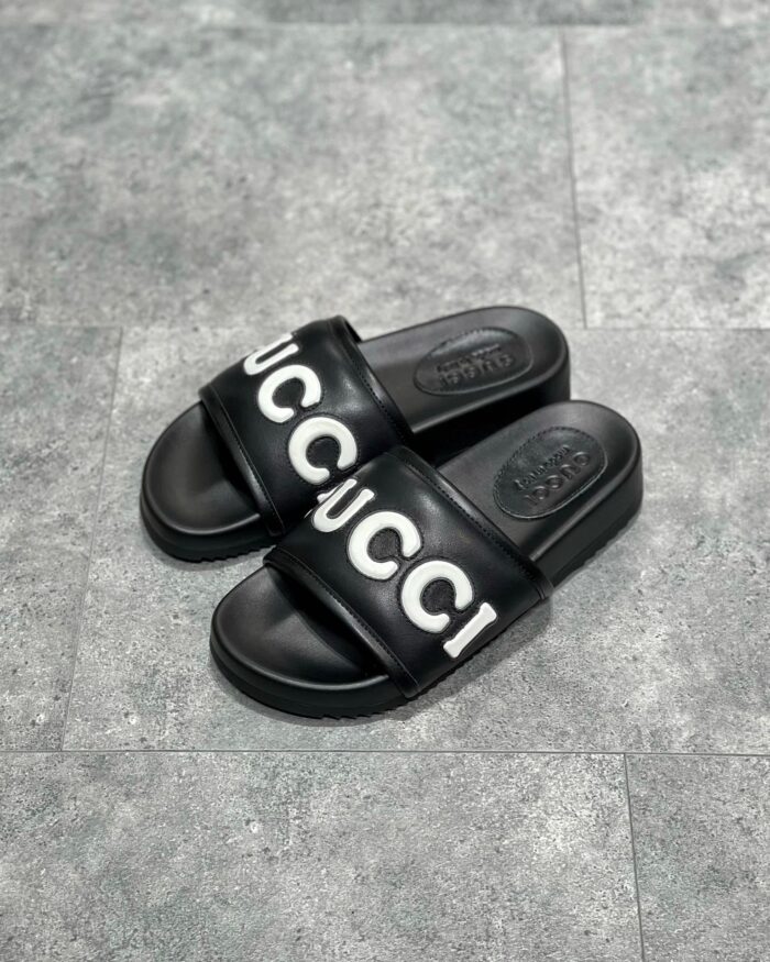 Sandali slide Gucci neri con logo bianco, stile casual e comfort di lusso.
