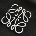 Ricamo bianco su tessuto scuro con monogramma elegante e dettagli raffinati.