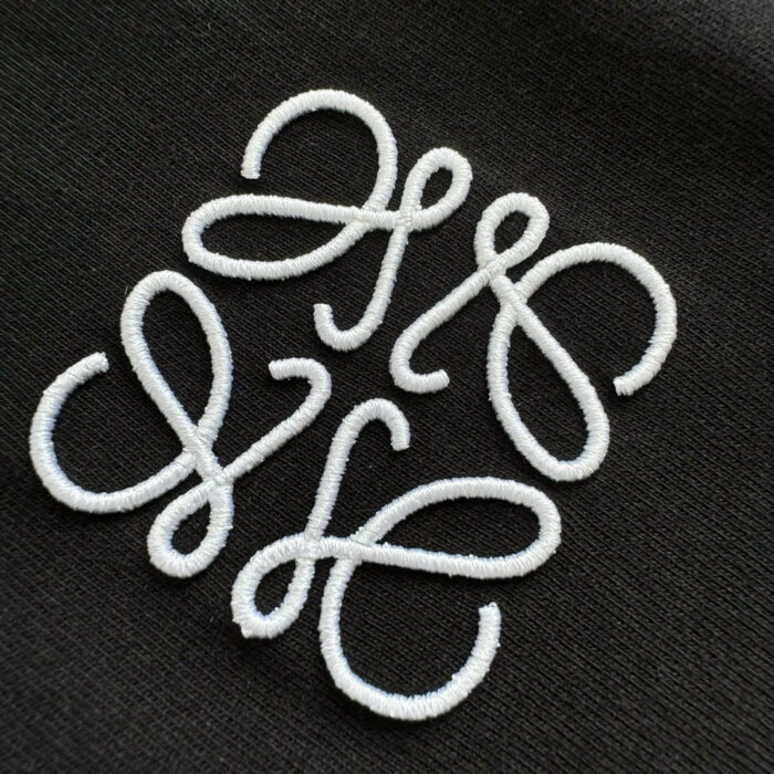 Ricamo bianco su tessuto scuro con monogramma elegante e dettagli raffinati.
