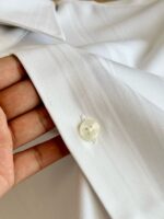 Dettaglio della manica di camicia bianca elegante e ben stirata, chiusa con bottone lucido.