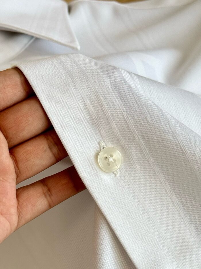 Dettaglio della manica di camicia bianca elegante e ben stirata, chiusa con bottone lucido.