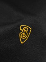 Emblema ricamato su tessuto nero, con scudo giallo e design stilizzato di spirale e numero 3.
