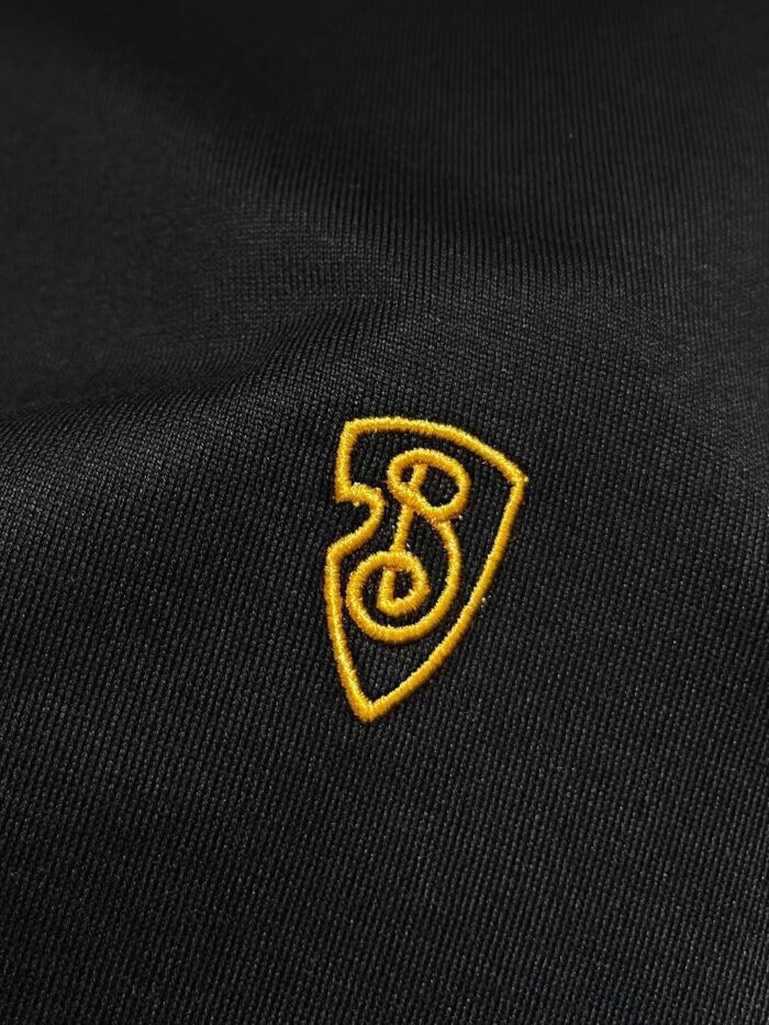 Emblema ricamato su tessuto nero, con scudo giallo e design stilizzato di spirale e numero 3.