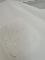 Dettaglio di tessuto bianco con logo embossato elegante e texture raffinata.