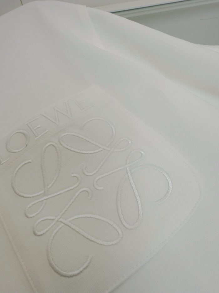 Dettaglio di tessuto bianco con logo embossato elegante e texture raffinata.