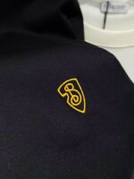 Logo ricamato su tessuto scuro di alta qualità, elegante e dettagliato, perfetto per abbigliamento premium.