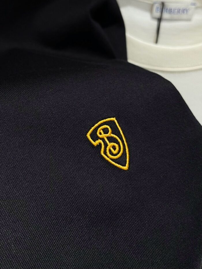 Logo ricamato su tessuto scuro di alta qualità, elegante e dettagliato, perfetto per abbigliamento premium.
