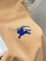 Top beige con ricamo di cavallo blu, elegante e versatile, perfetto per look casual e di tendenza.