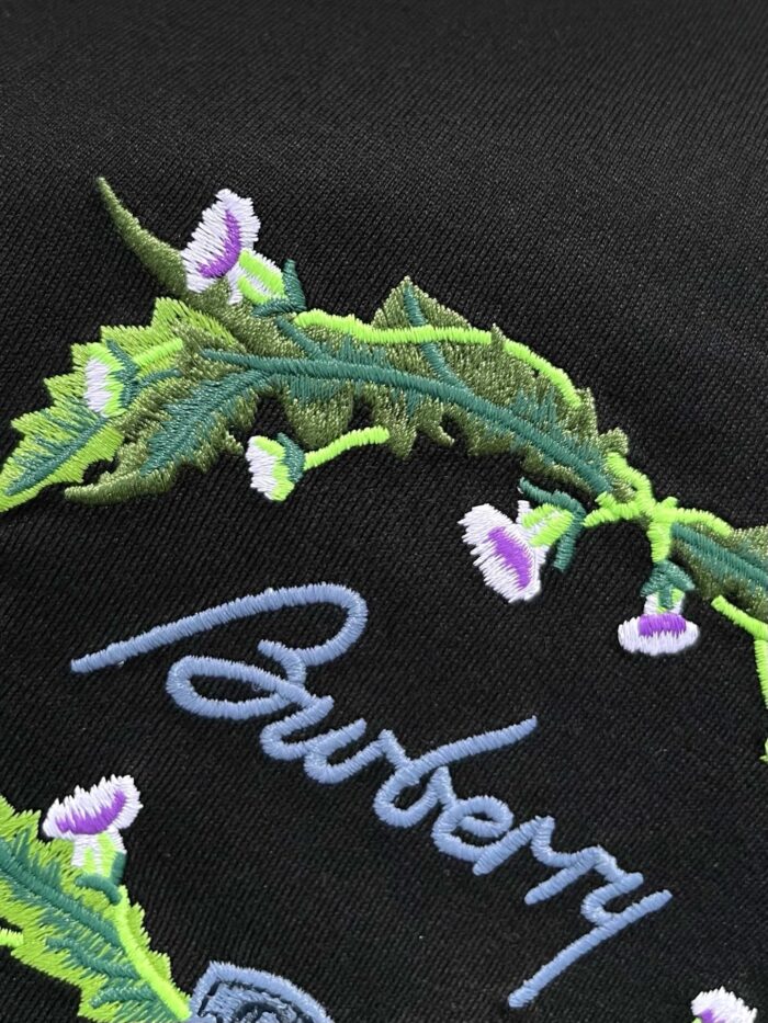 Ricamo Burberry elegante con logo blu e dettagli floreali su tessuto nero.