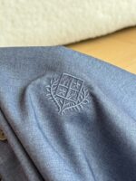 Emblema ricamato su giacca grigia elegante, tessuto di alta qualità e dettagli raffinati.