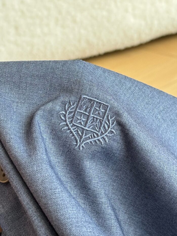 Emblema ricamato su giacca grigia elegante, tessuto di alta qualità e dettagli raffinati.
