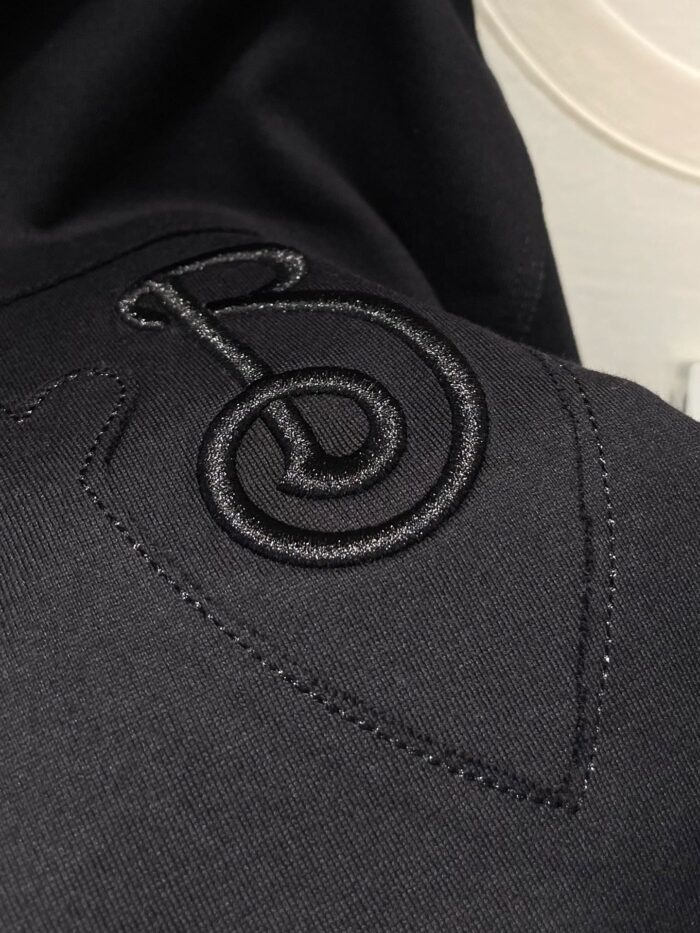 Maglia nera con ricamo musicale elegante, tessuto lucido e dettagli discreti di stile sofisticato.
