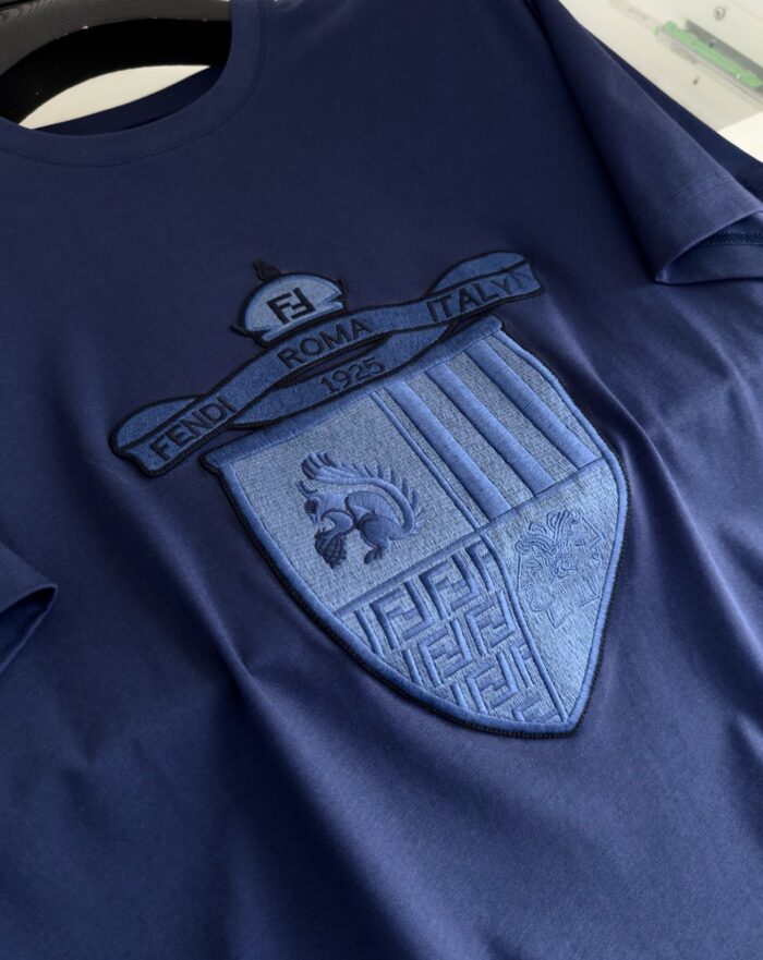 Maglietta navy blu con logo ricamato e stemma dettagliato, stile elegante e casual.
