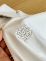Camicia bianca con ricamo di stemma e dettagli floreali eleganti, perfetta per stile e prestigio.